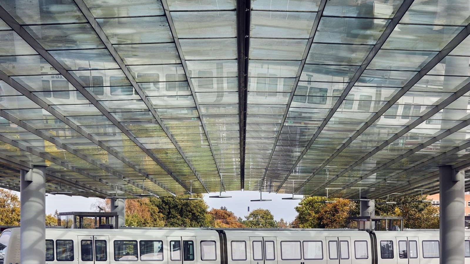 En hvid metro holder ved en perron overdækket af et stort glastag.